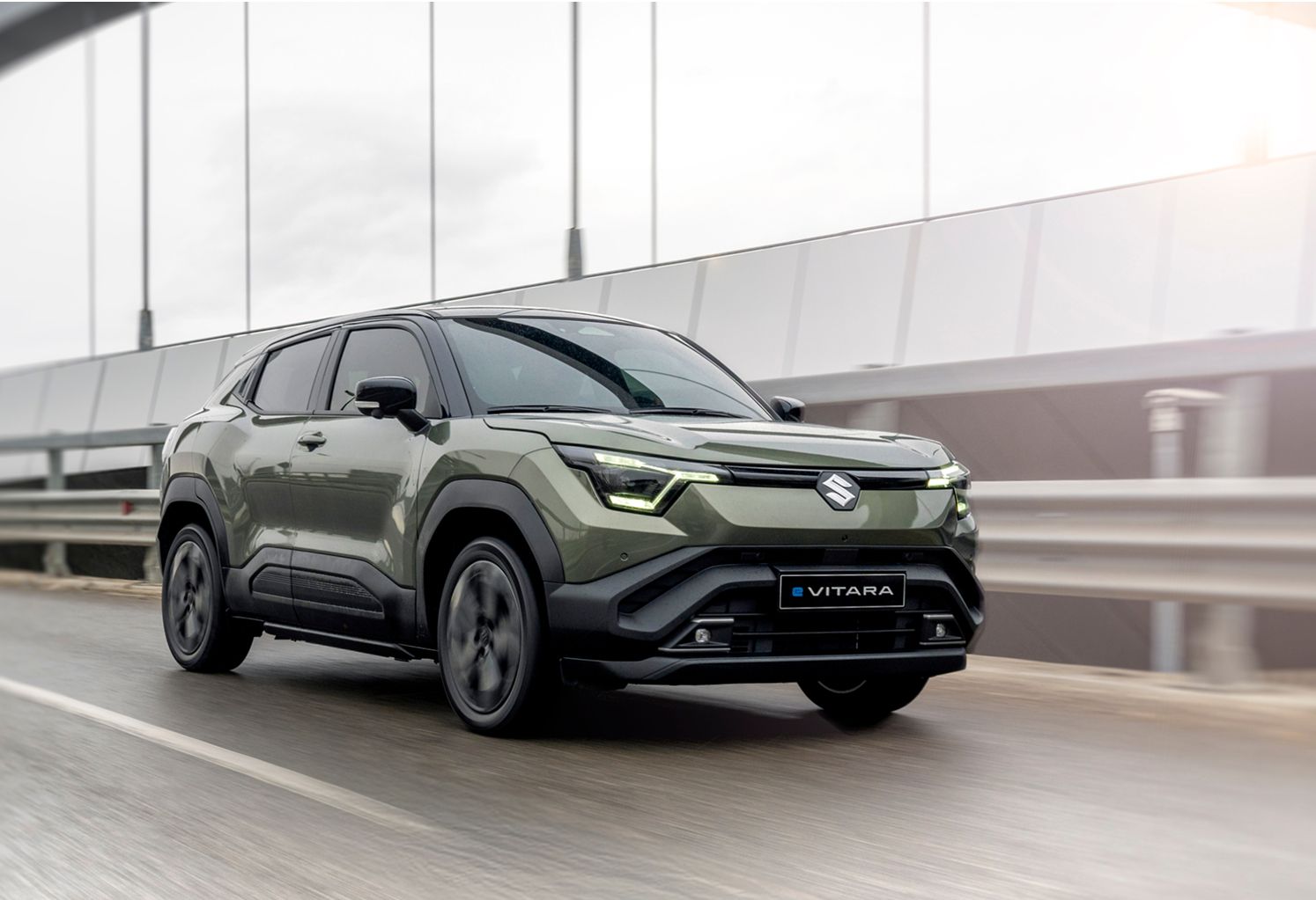 Olivegrüner Suzuki e VITARA in Front-Seitenansicht auf einer Brücke