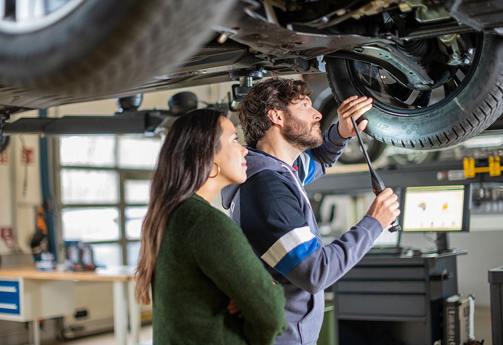 Ein Mann und eine Frau befinden sich bei einem Servicetermin unterhalb eines Fahrzeugs auf einer Hebebühne.