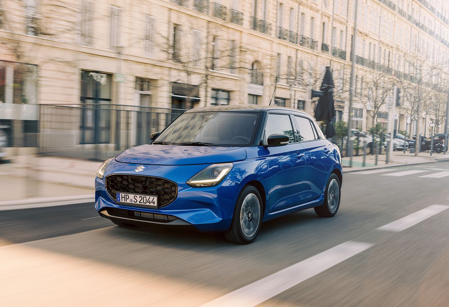 Blauer Suzuki Swift fährt auf städtischer Straße.