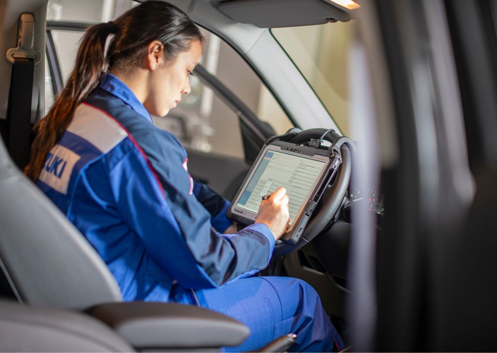 Eine Kfz-Mechatronikerin sitzt in einem Fahrzeug und wertet ein Messgerät aus