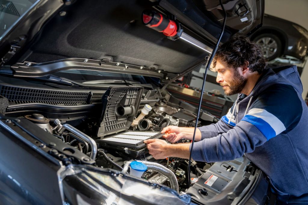 Ein Kfz-Mechatroniker tauscht im Motorraum eines Fahrzeugs einen Filter aus