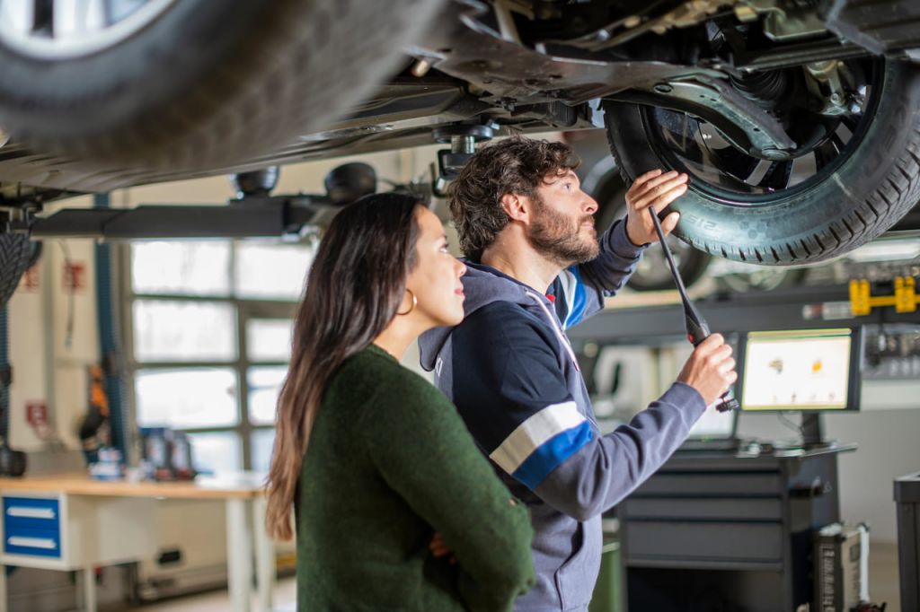 Ein Kfz-Mechatroniker mit Kundin unter Fahrzeug auf Hebebühne
