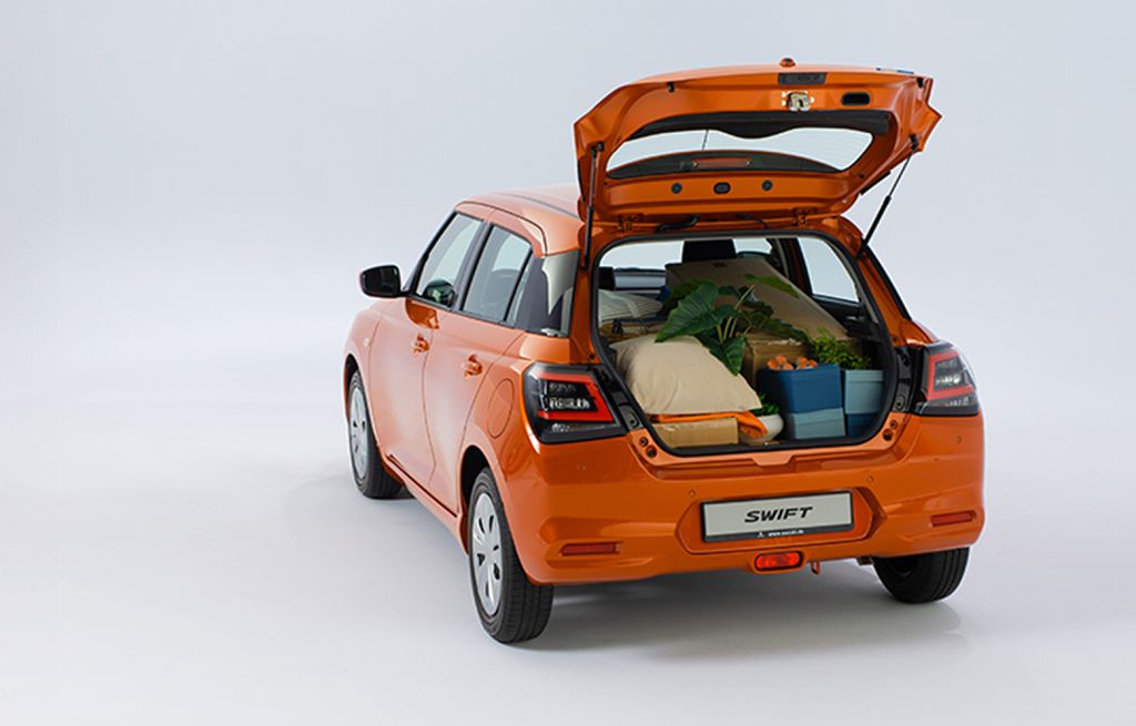 Der Suzuki Swift in orange steht mit geöffnetem und beladenem Kofferraum vor einem neutralen weißen Hintergrund.
