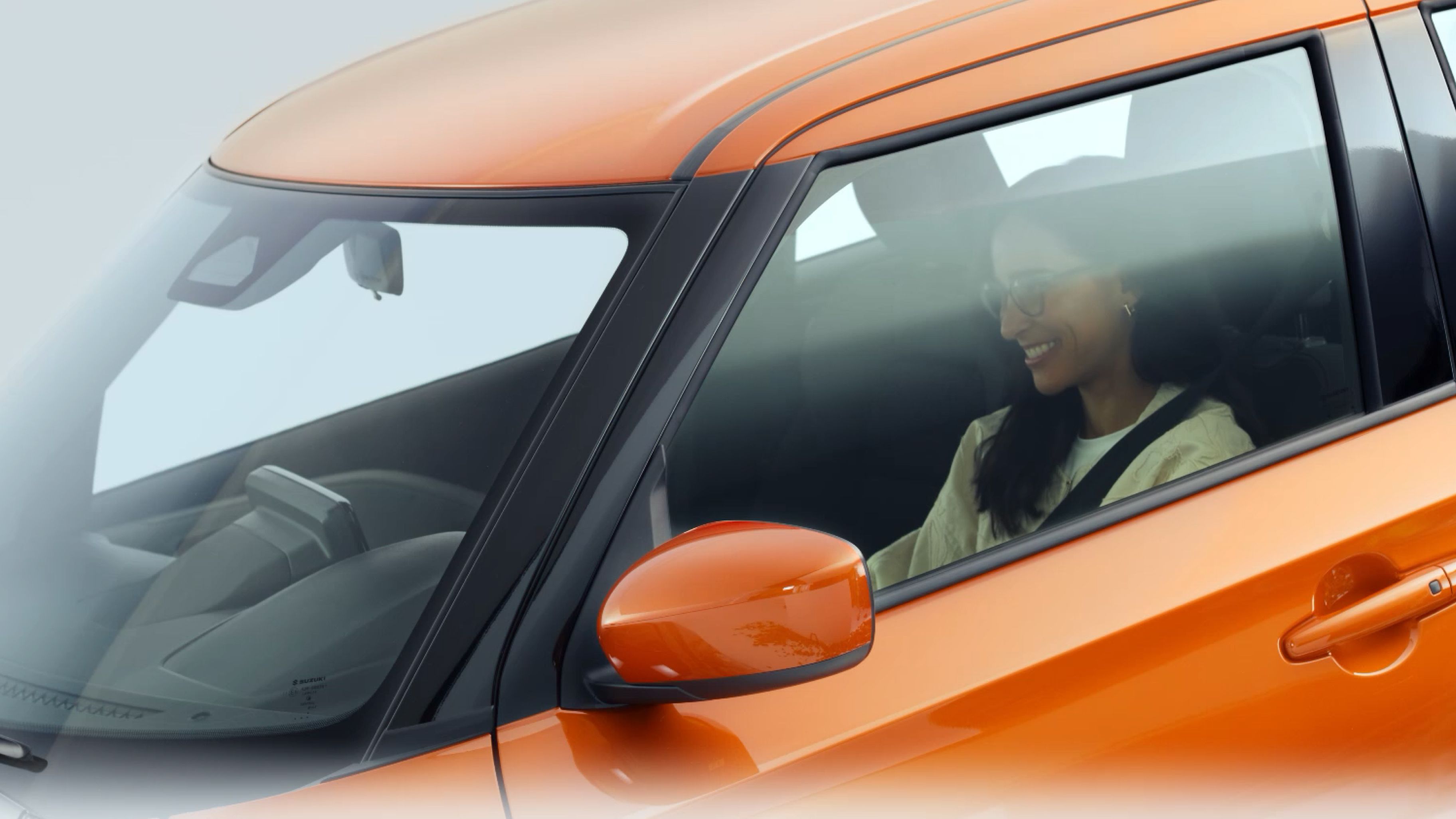 Eine Frau sitzt am Steuer eines orangenen Suzuki Swift.